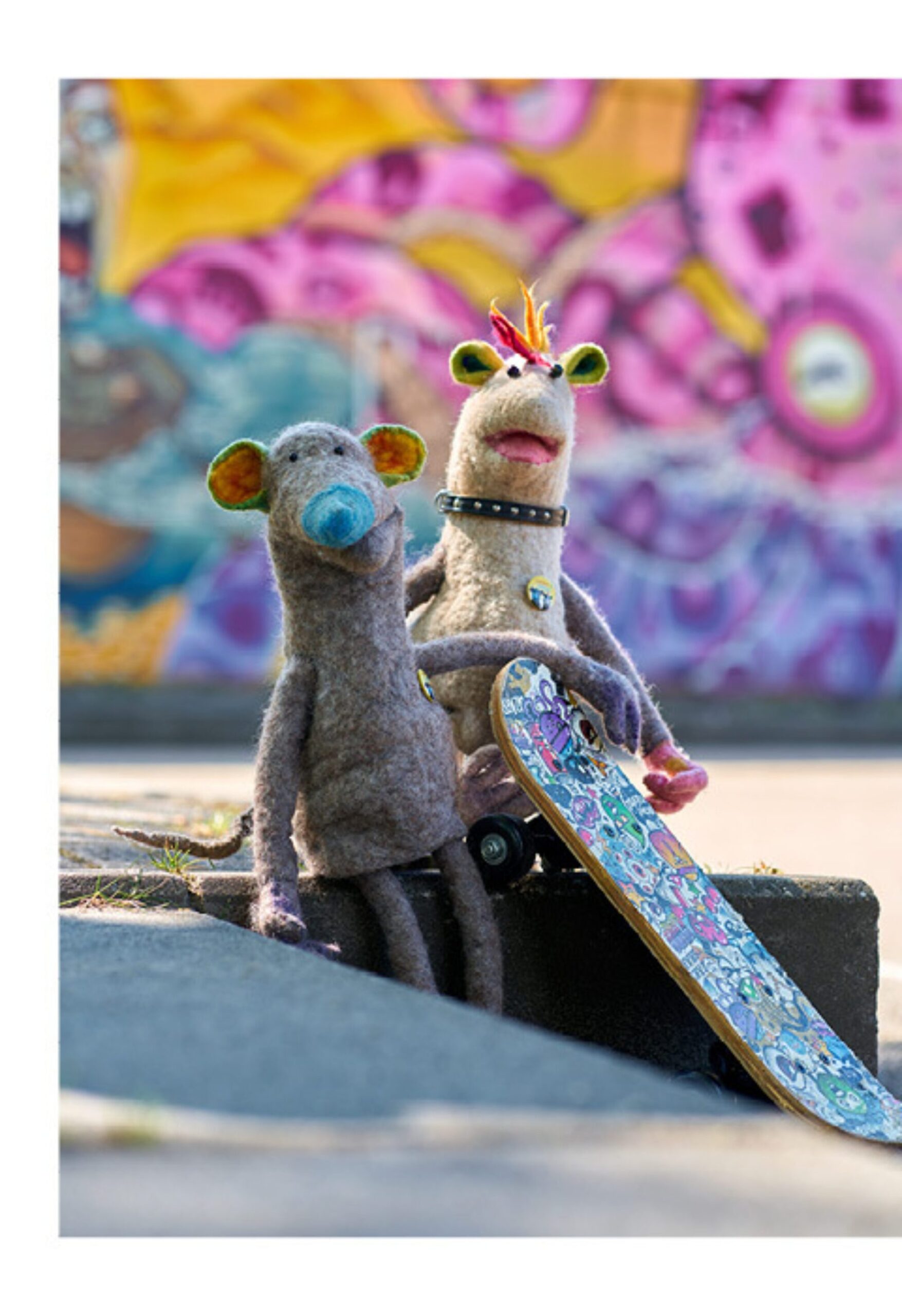 Campagnebeeld met twee poppen op een skatebord voor een kleurrijke muur
